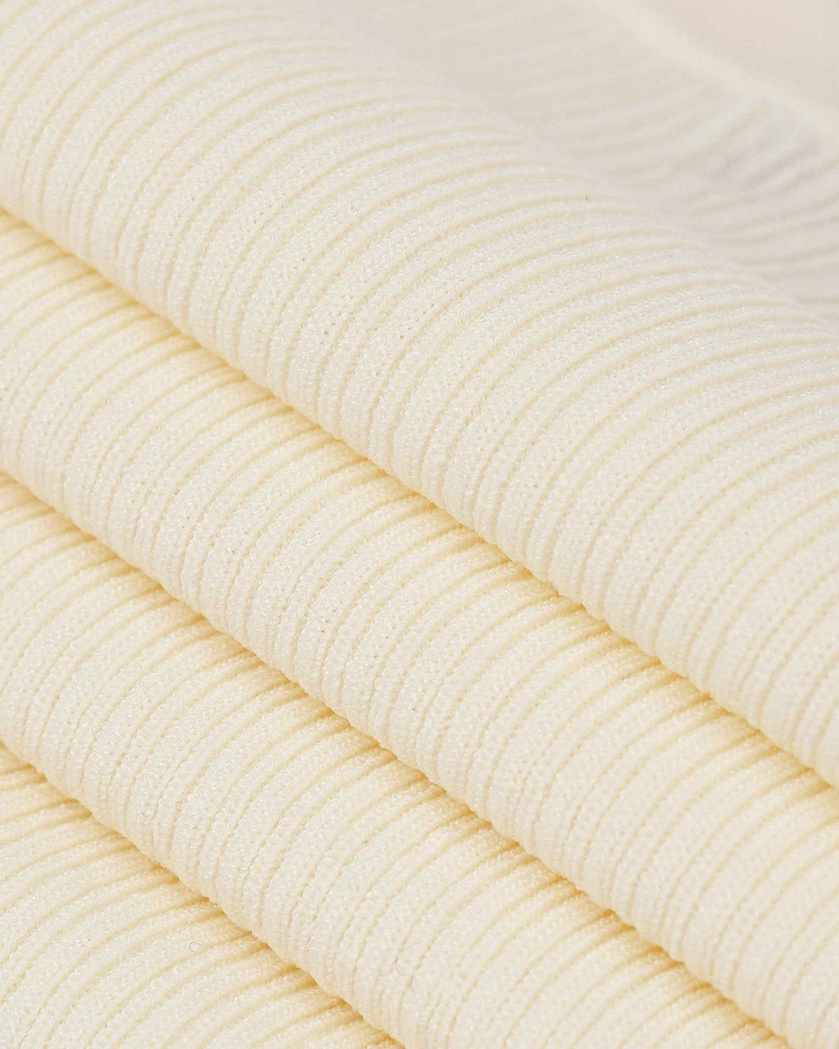 Fine ribs become visible across the folded ivory knit, creating alternating lines of light and shadow.