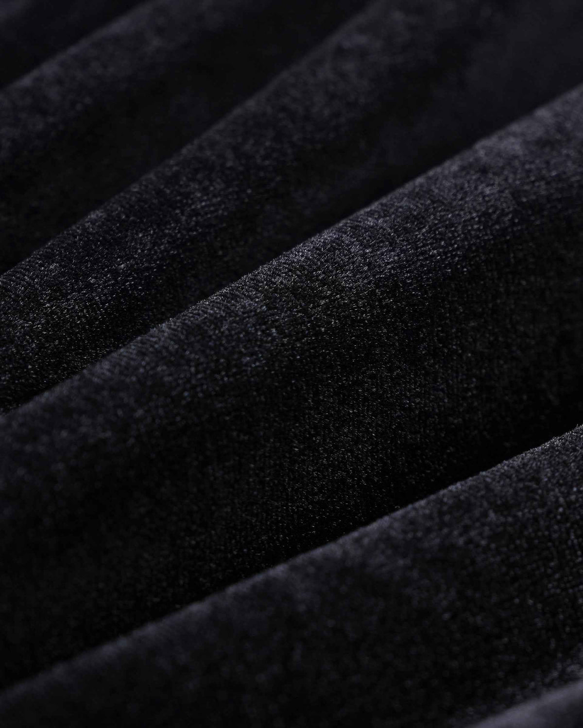 Fine surface texture catches the light along the folds, shifting between deeper black and softer highlights.