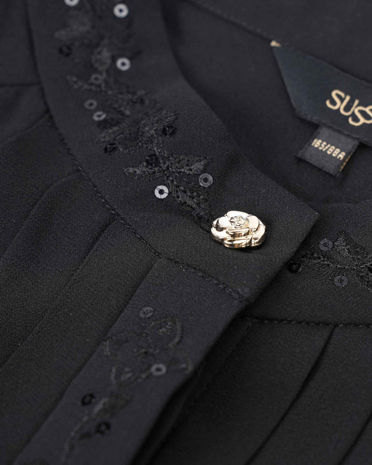 Tiny reflective accents follow the collar beside a decorative button, bringing light to the black fabric.