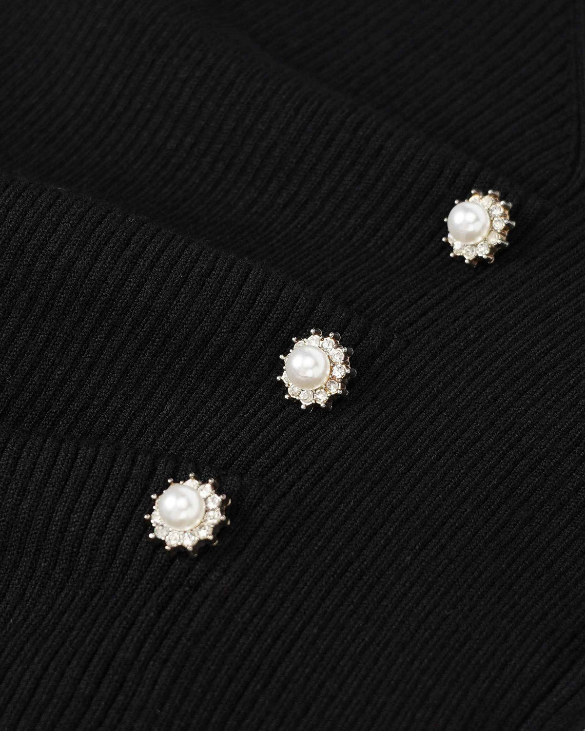 Three pale, flower-like buttons punctuate the black ribbed knit.