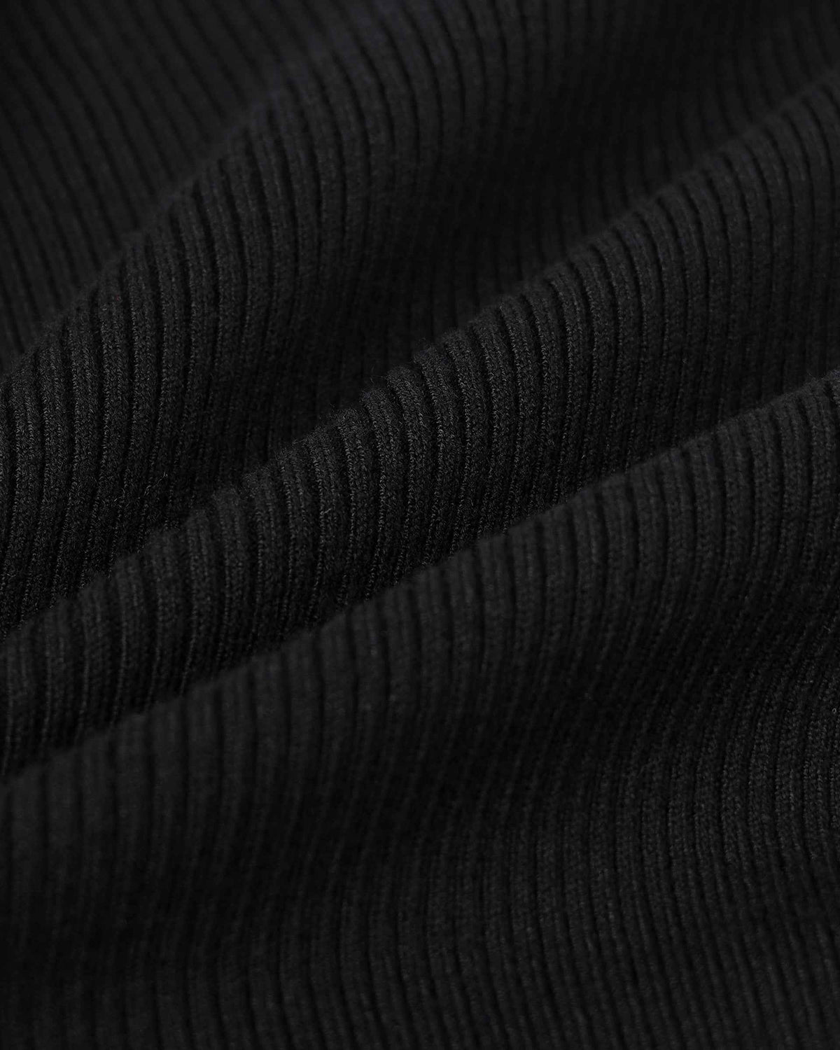 Narrow ribs cross the folded black knit, creating a fine pattern of highlights and shadows.