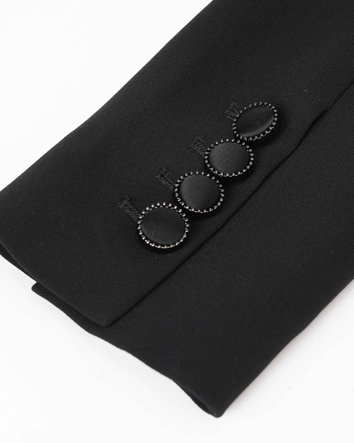 A row of dark buttons finishes the blazer's cuff, with fine edging visible around each one.