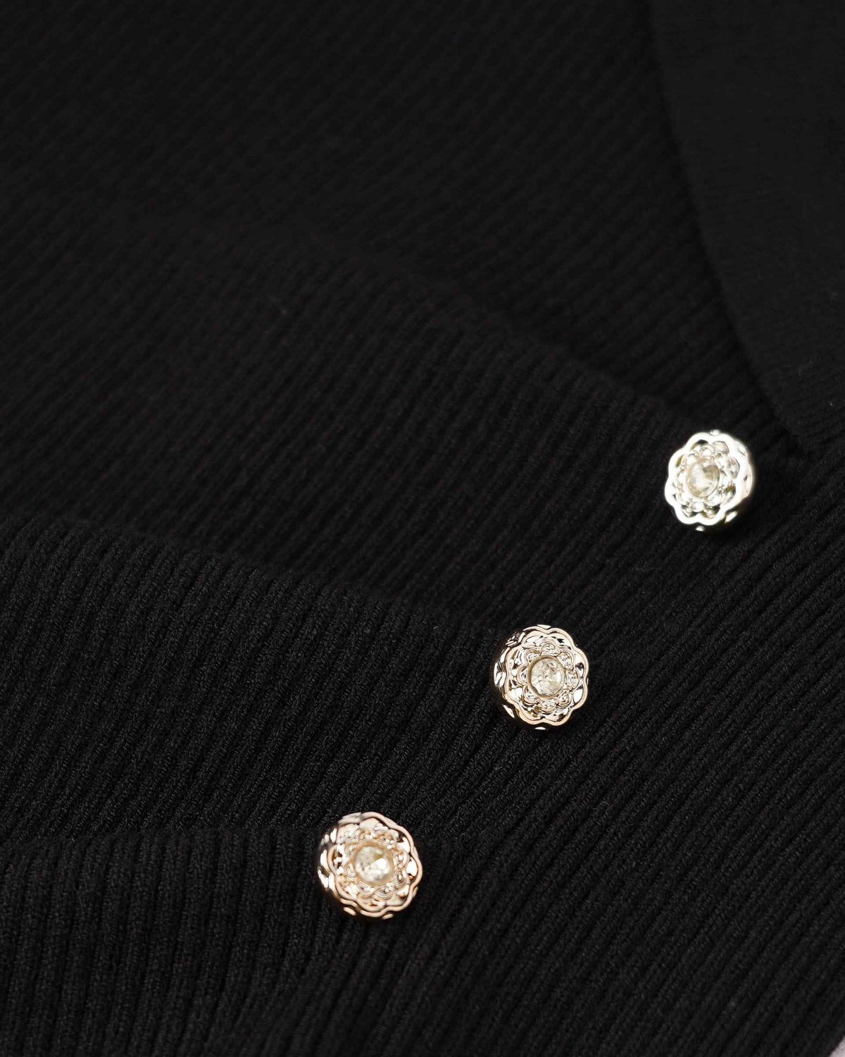 Small, rounded decorative buttons punctuate the dark knit beside the shaped front.