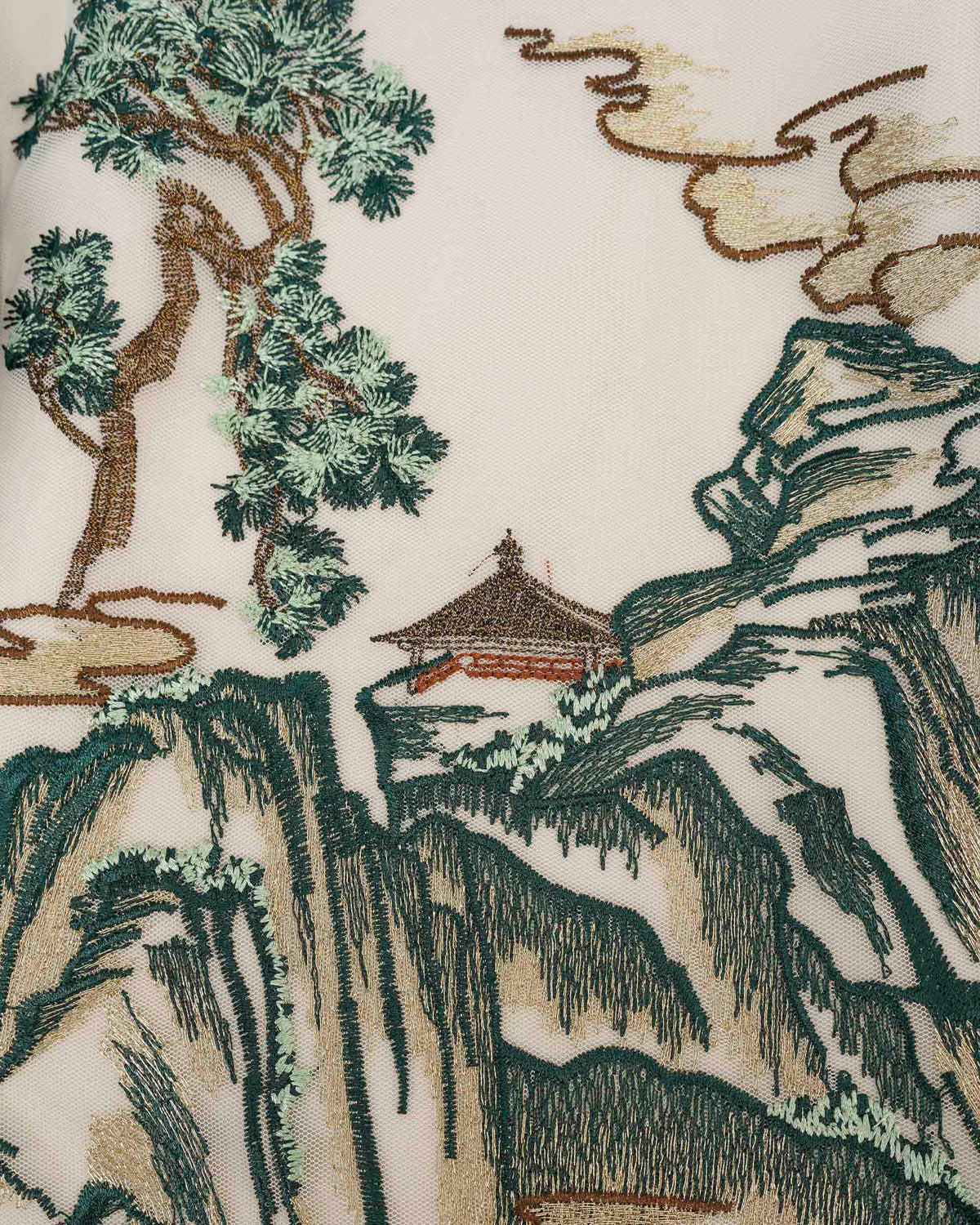Trees, mountains, and a small architectural form appear within the pale embroidered panel.