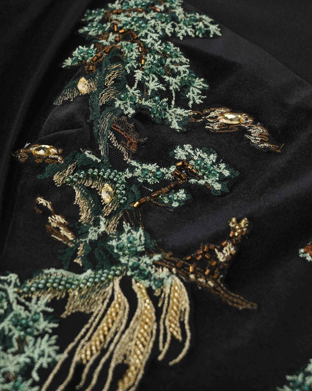 Green trees and flowing gold-toned lines form an embroidered landscape against black.