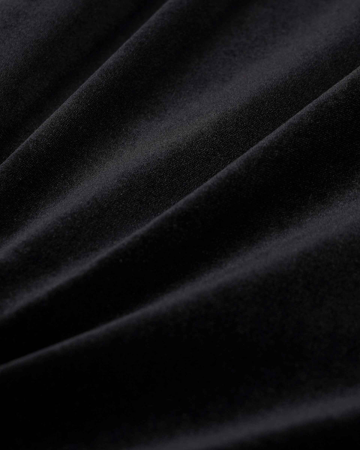 Light passes across the folded dark fabric, revealing subtle highlights and deep shadows.