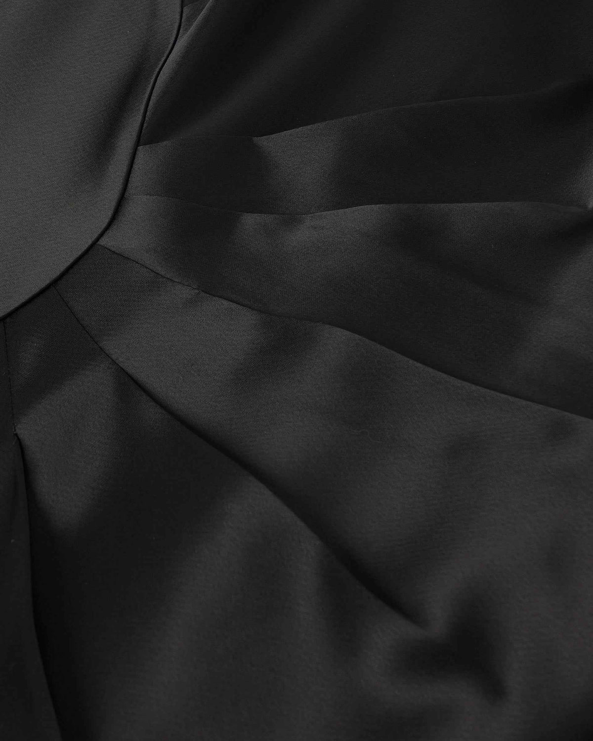 Broad folds move diagonally across the dark fabric, creating a concentrated change in light and shadow.