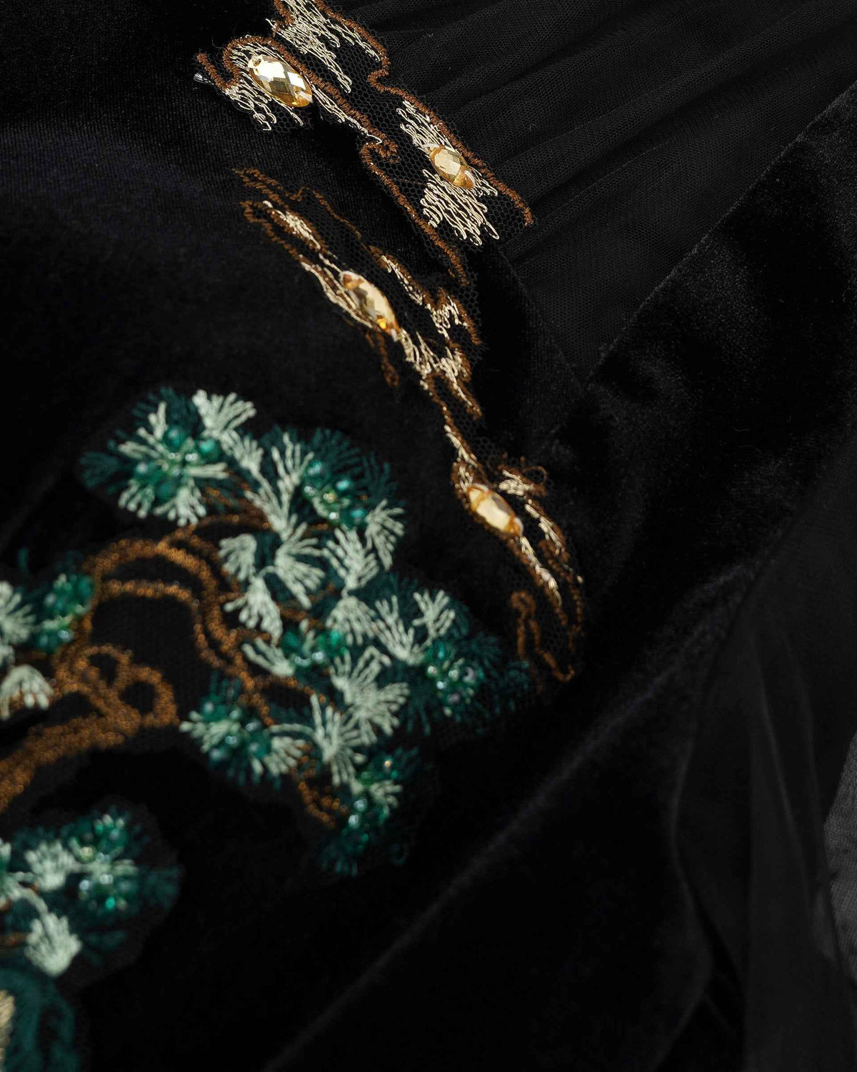 Pale and deep green threads distinguish the leaves from the darker ground, while gold-toned accents trace nearby forms.