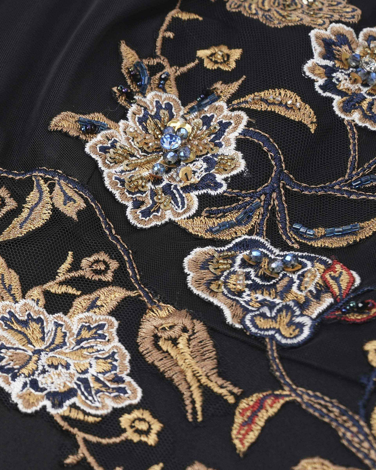 Blue, ivory, and gold-toned threads build distinct outlines within the floral embroidery.