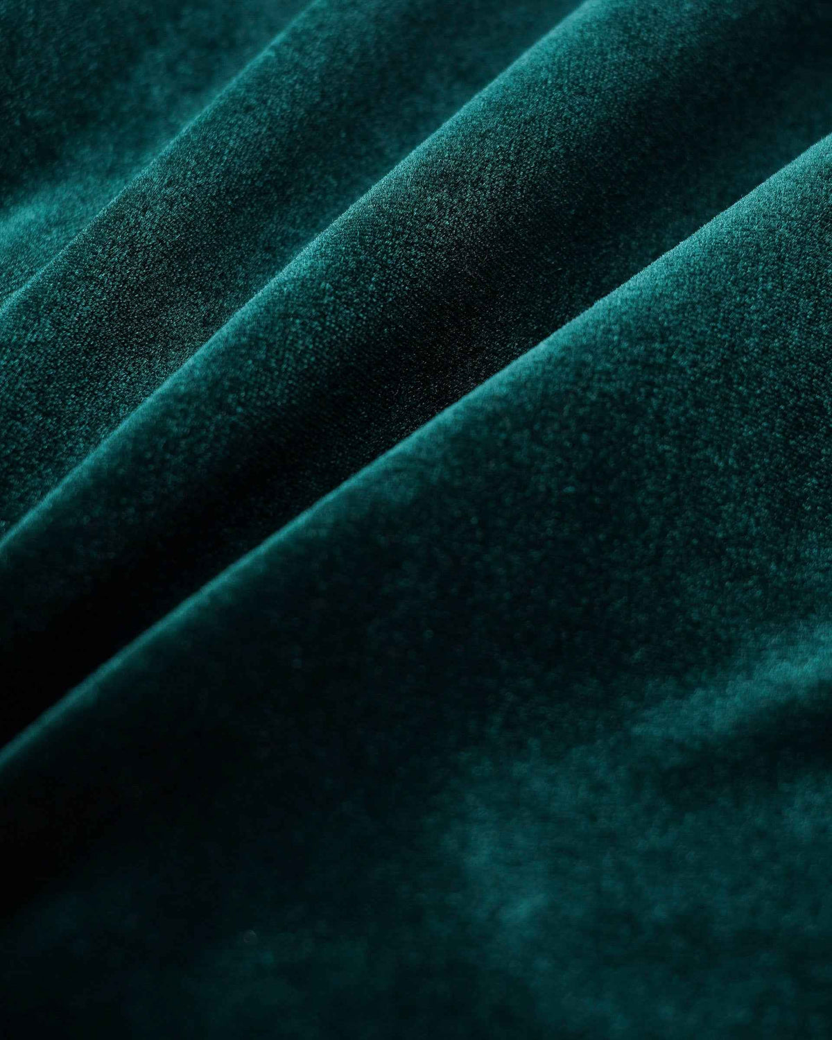 The velvet's fine pile catches light across the folds, moving between bright green highlights and darker shadows.