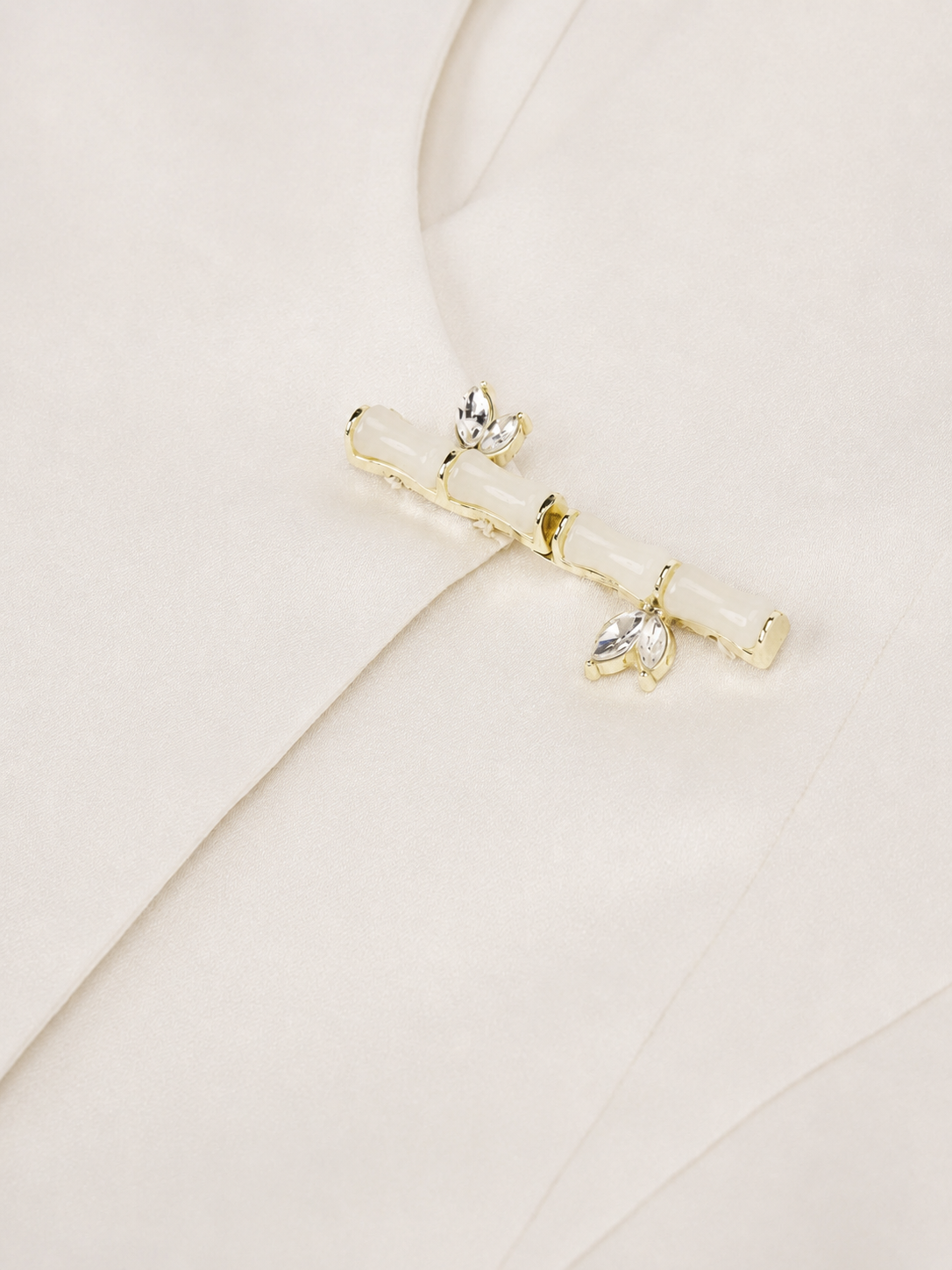 A pale bamboo-inspired clasp bridges the ivory front, with small leaf-like details beside its segmented form.