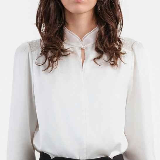 The blouse's small collar and long sleeves frame a softly shaped upper body.