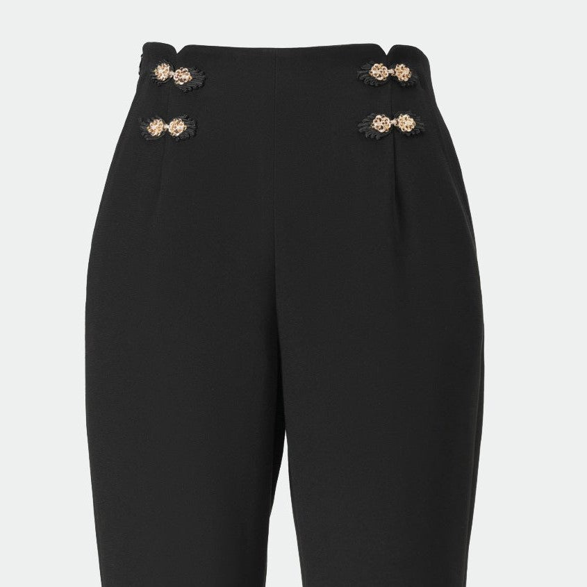 Pale decorative accents sit near the waistband on either side of the black trousers.